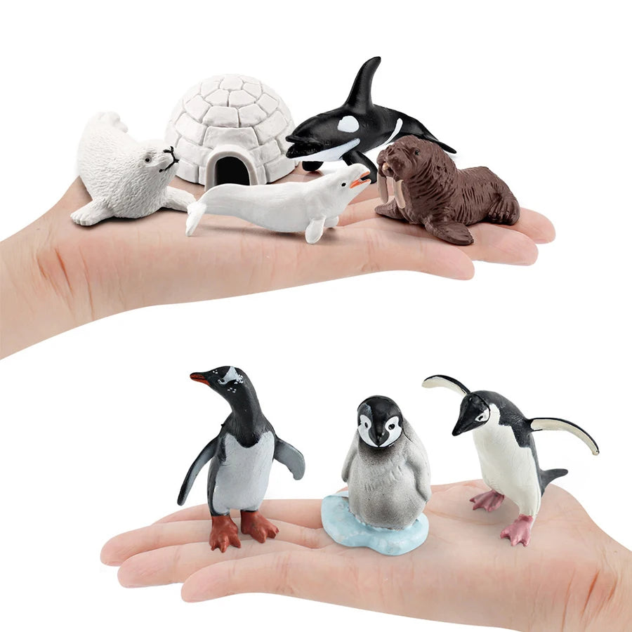 A hand holds a set of realistic mini ocean animal figurines including a whale, shark, dolphin, turtle, and penguin.
