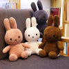 A collection of Miffy plush toys in various colors including brown, white, and gray, displayed on a dark surface.