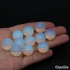 A hand holds several smooth, translucent crystal spheres displaying natural pink and yellow internal light.