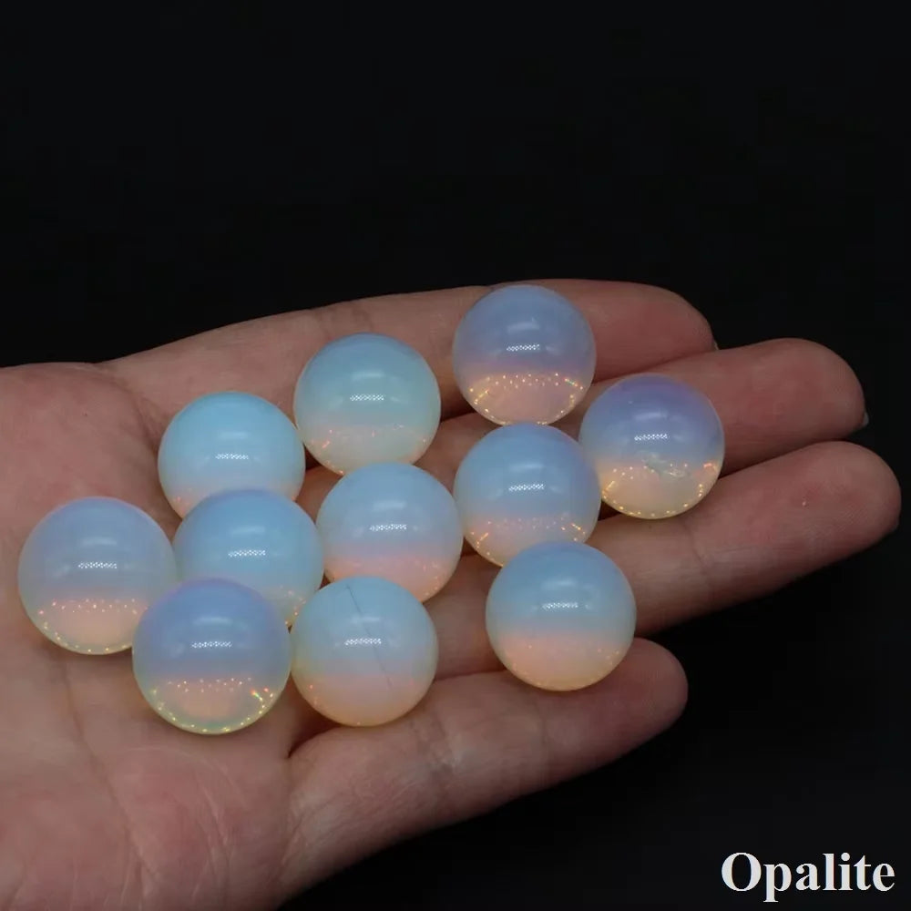 A hand holds several smooth, translucent crystal spheres displaying natural pink and yellow internal light.