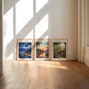 Trois tirages de paysages encadrés, intitulés Velaris Lunathion et Terrasen, exposés sur un mur clair.