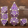 A set of seven polyhedral metal dice in purple and silver, displayed on a wooden surface.