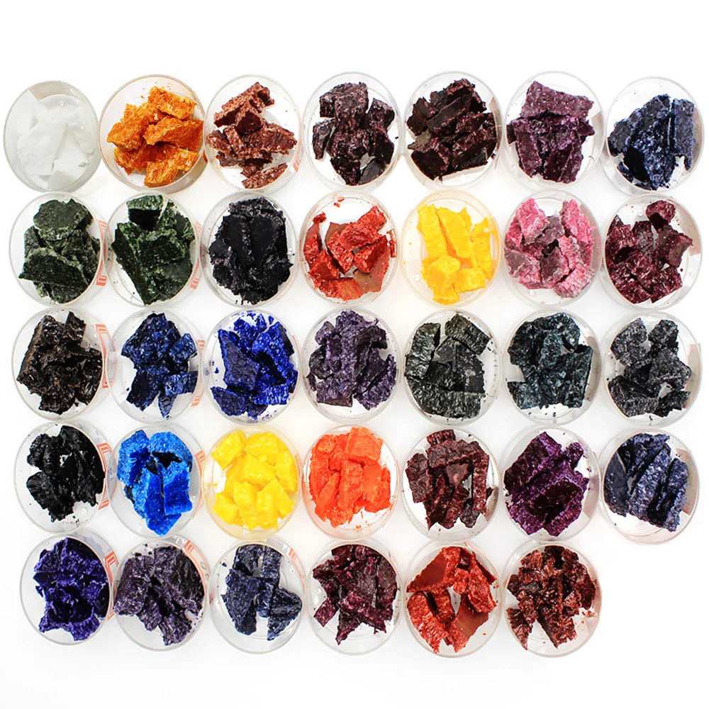A collection of colorful candle dye chips in various shades including black, purple, blue, yellow, and red.