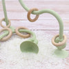 A soft silicone teether ring in light green and natural wood tones resting on a white textured surface.