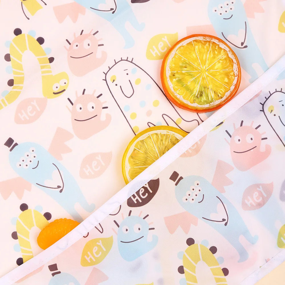 A close-up of a 2-pack of waterproof full sleeve baby bibs featuring cute yellow and orange citrus fruit designs on a light b