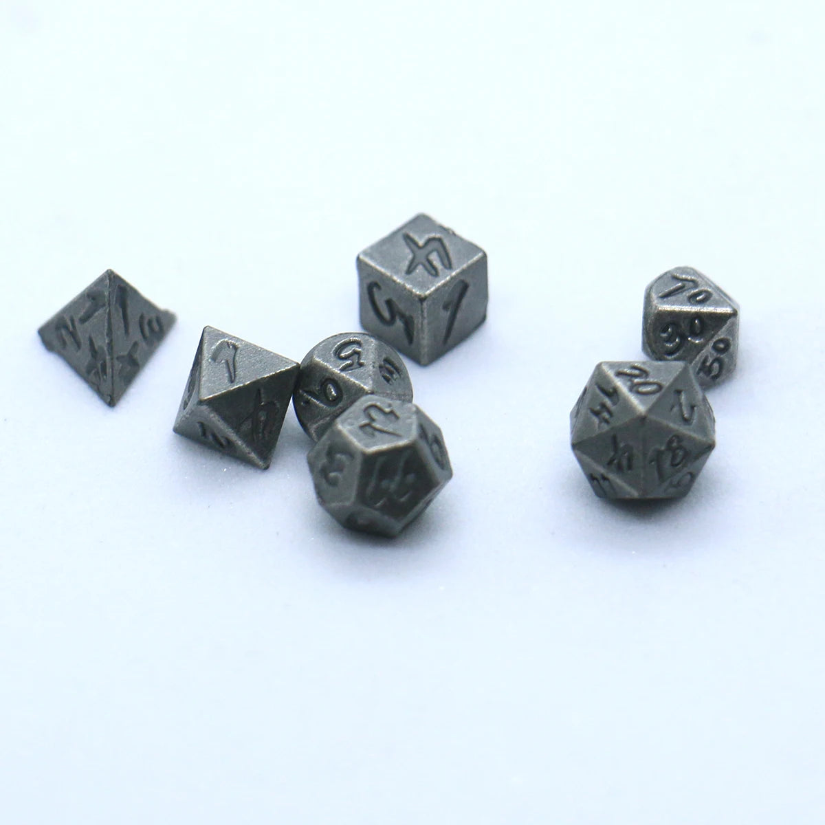 A set of seven antique metal polyhedral dice, including a d4, d6, d8, d10, d12, d20, and d100.