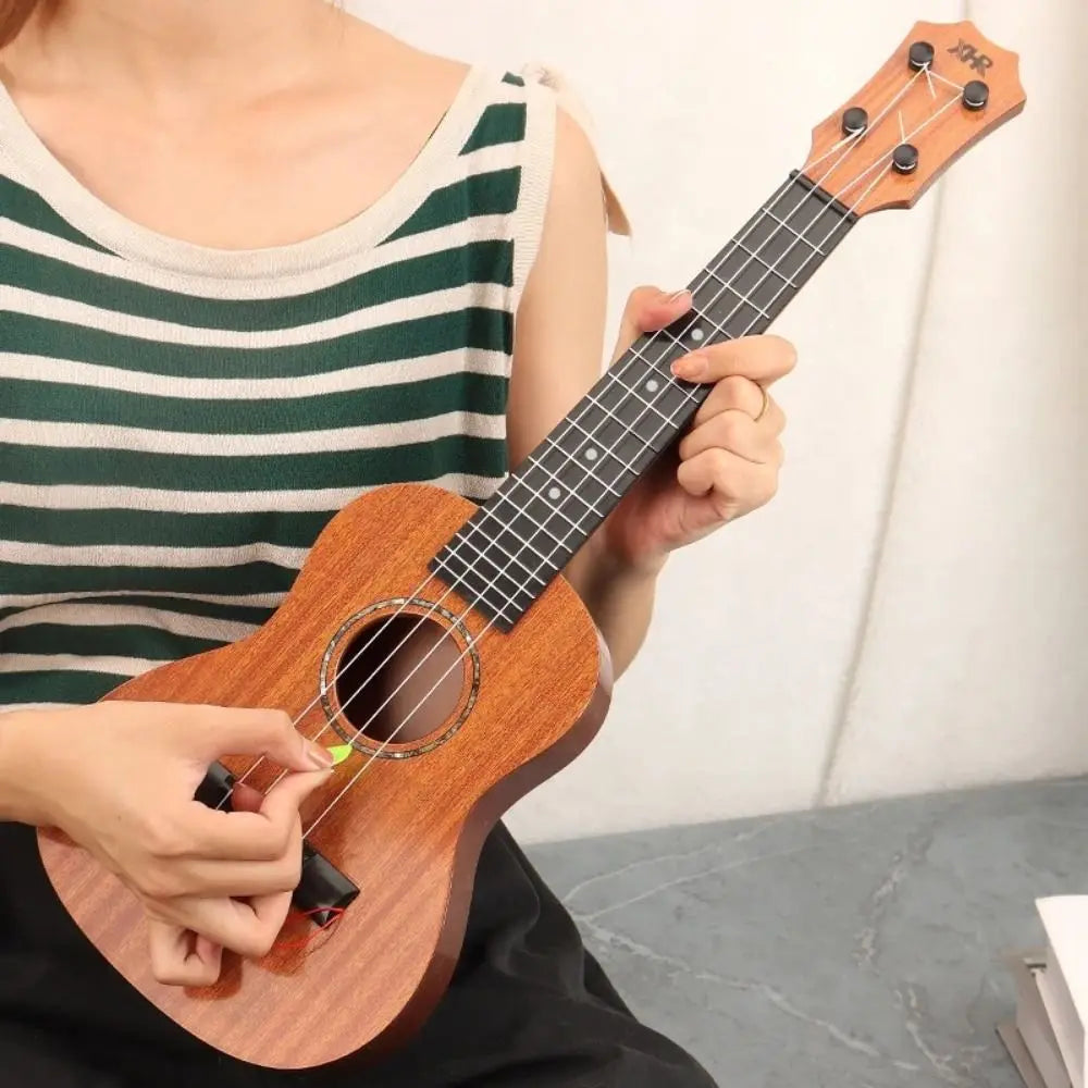 A person holds a wooden ukulele toy with adjustable tuning pegs and a light-colored striped shirt.