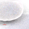 A close-up view of clear, iridescent glass seed beads scattered on a white dish.
