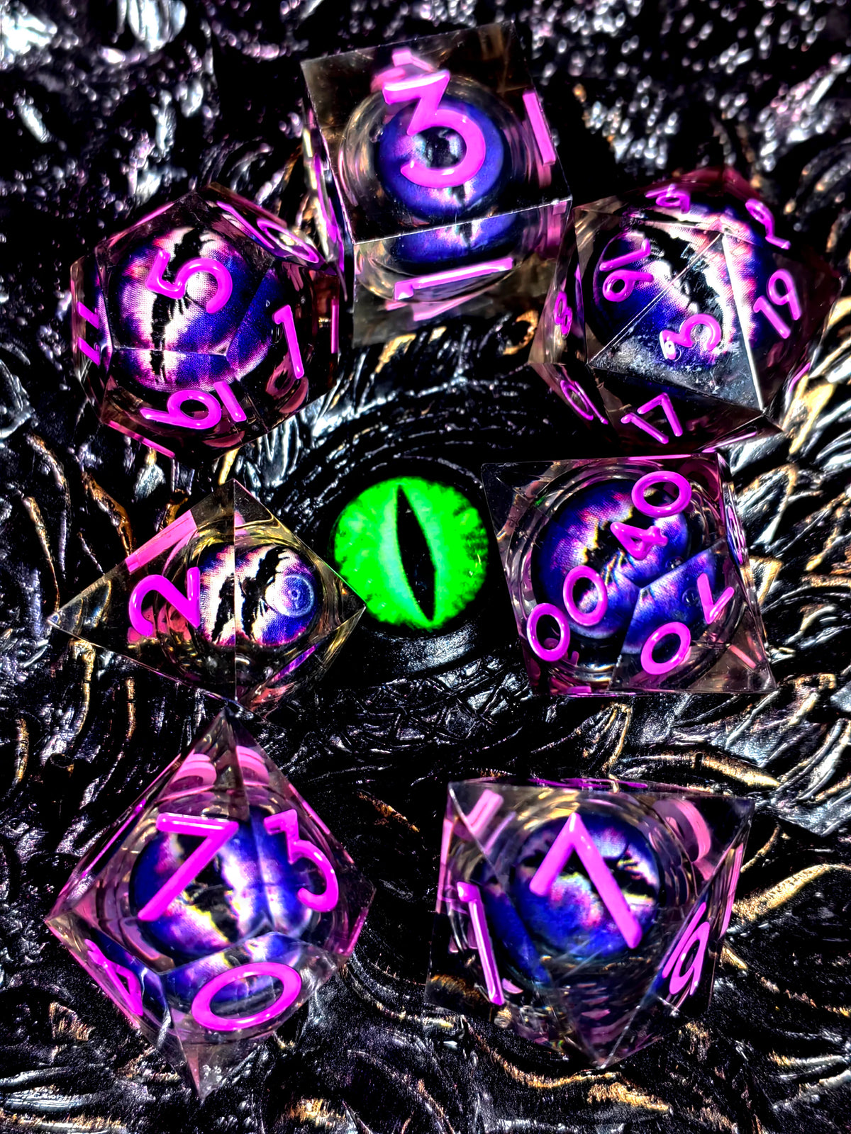 A collection of iridescent resin dice with spinning dragon eye cores scattered on a dark, textured surface.