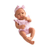 A lifelike vinyl reborn doll with a pink outfit and bow, shown in a natural pose.