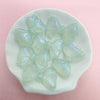 A collection of translucent, pale green shimmer mermaid bowknot beads arranged on a white dish.