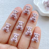 A hand holds several small, fuzzy pink resin teddy bear charms for DIY crafts.