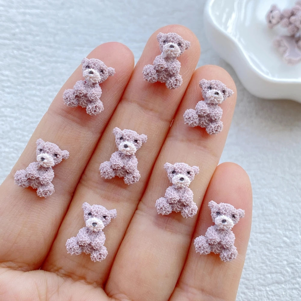 A hand holds several small, fuzzy pink resin teddy bear charms for DIY crafts.