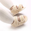 Pair of beige breathable first walker sandals for baby with hook-and-loop closure shown on a leg.