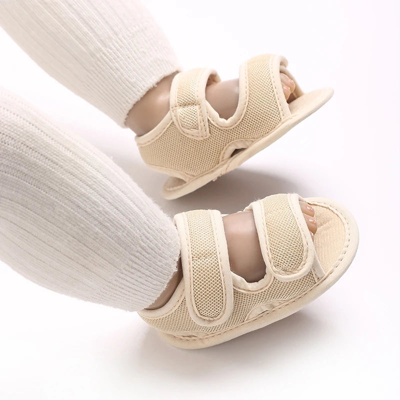 Pair of beige breathable first walker sandals for baby with hook-and-loop closure shown on a leg.