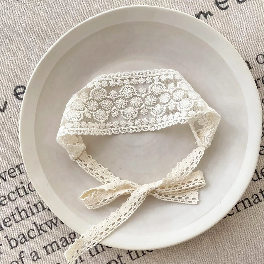 White floral lace baby headband for newborns displayed on a light ceramic plate.