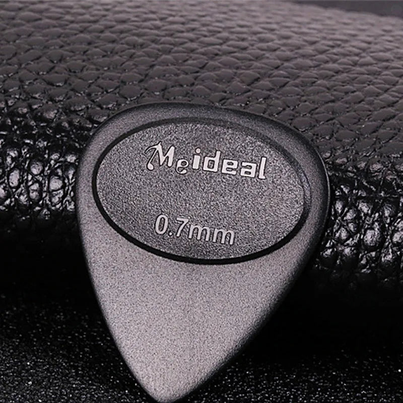 A close-up of a gray non-slip guitar pick labeled Meideal 0.7mm resting on a black surface.