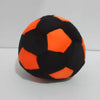 A black and orange crochet hacky sack ball resting on a white surface.