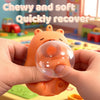 Hands hold an orange capybara squeeze toy with a clear bubble, demonstrating stress relief and recovery.