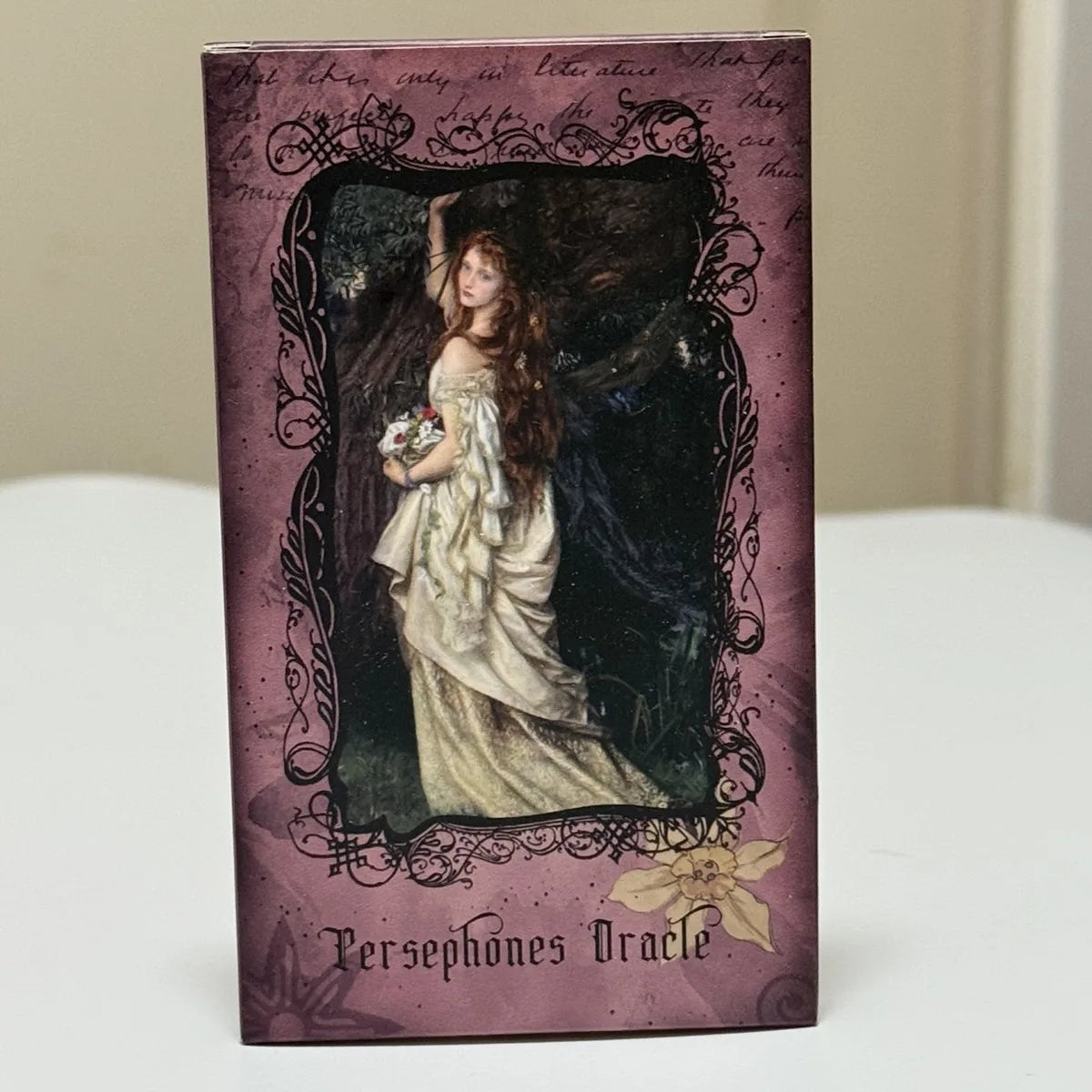 A dark purple deck of cards featuring a woman with long hair and flowers, titled Persephone Oracle.