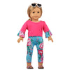 A doll wearing a pink unicorn pajama set with floral print leggings and sunglasses.