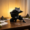 A black 3D printed samurai warrior figurine with a sword is displayed on a wooden surface next to white gravel.