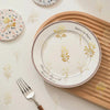 A white plate with a gold botanical design is placed on a wooden board, with silverware nearby.