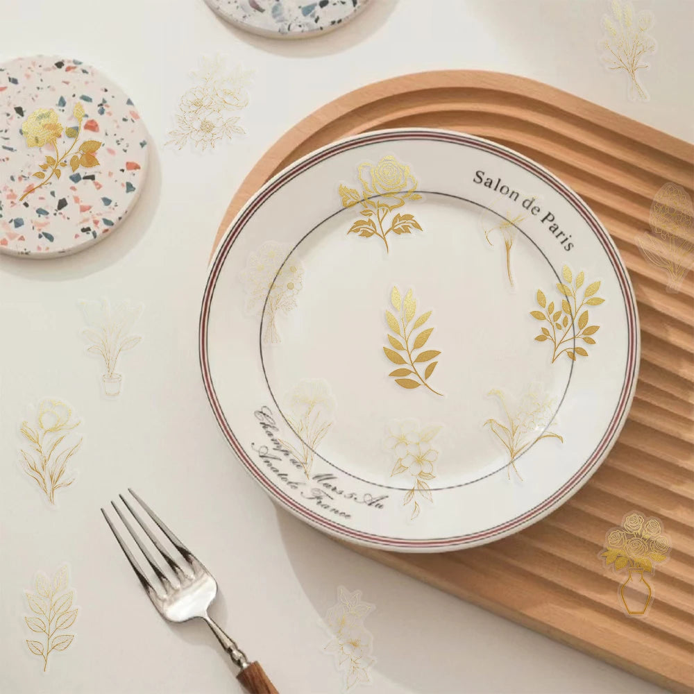 A white plate with a gold botanical design is placed on a wooden board, with silverware nearby.