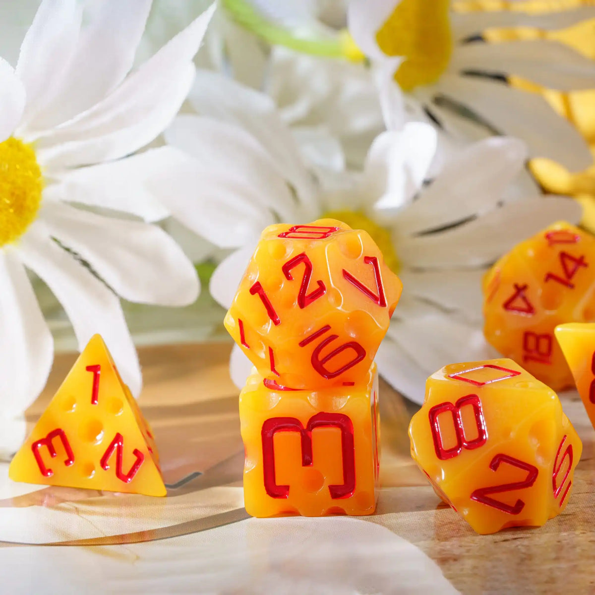 A set of seven cheese-themed polyhedral dice in yellow and orange colors resting on a wooden surface surrounded by white flow