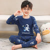 A young boy wearing a navy blue cotton pajama set with an astronaut print, sitting on the floor.