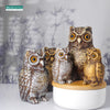 A group of realistic owl garden statues in various sizes and shades sitting on a white surface.