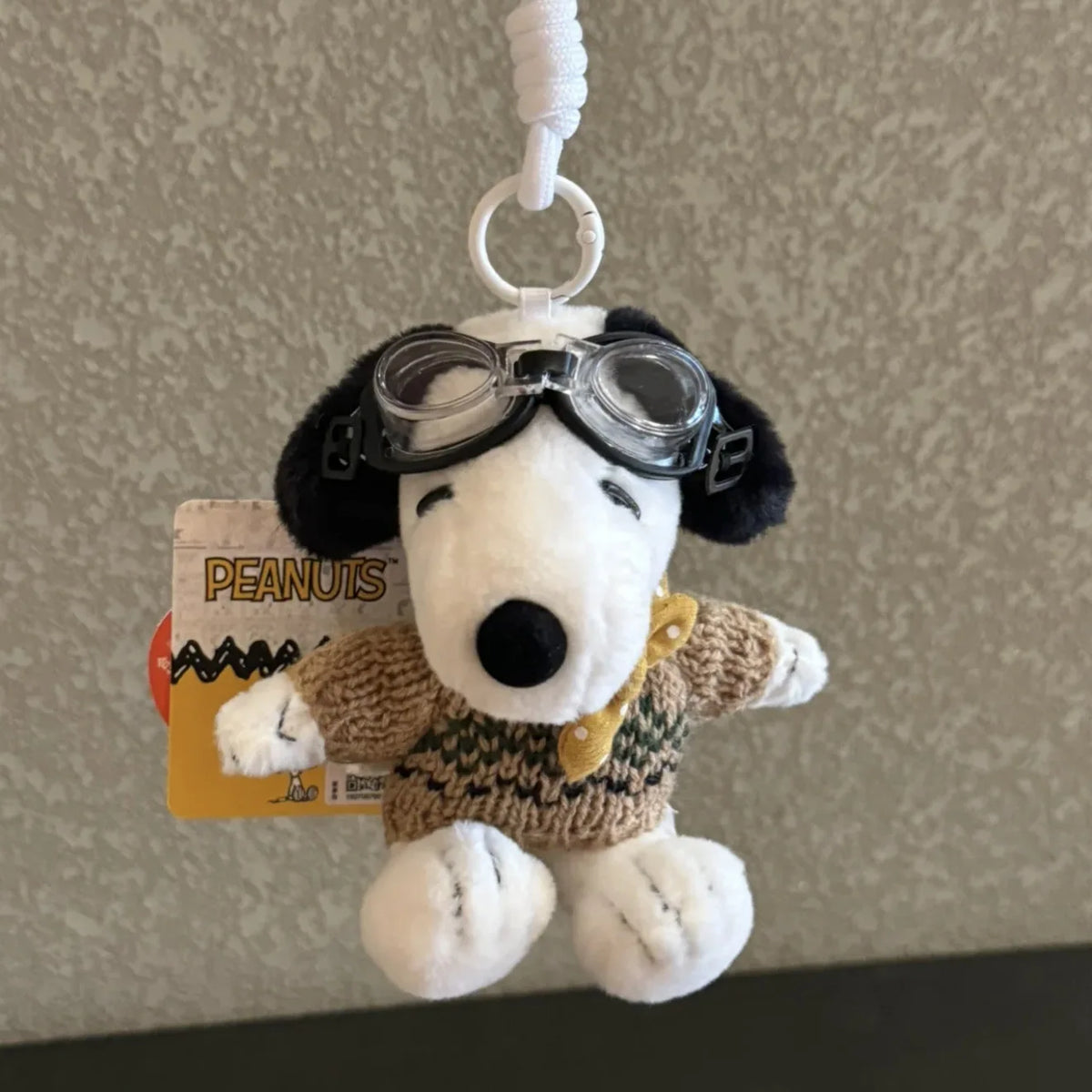 A white plush dog wearing black goggles, attached to a white cord for a keychain charm.