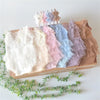 A display of various pastel lace baby rompers and matching headbands arranged in a wooden box.