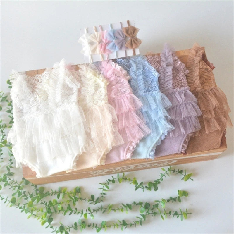 A display of various pastel lace baby rompers and matching headbands arranged in a wooden box.