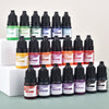 A collection of dark glass dropper bottles filled with various liquid candle and soap colorants in shades of green, yellow, p