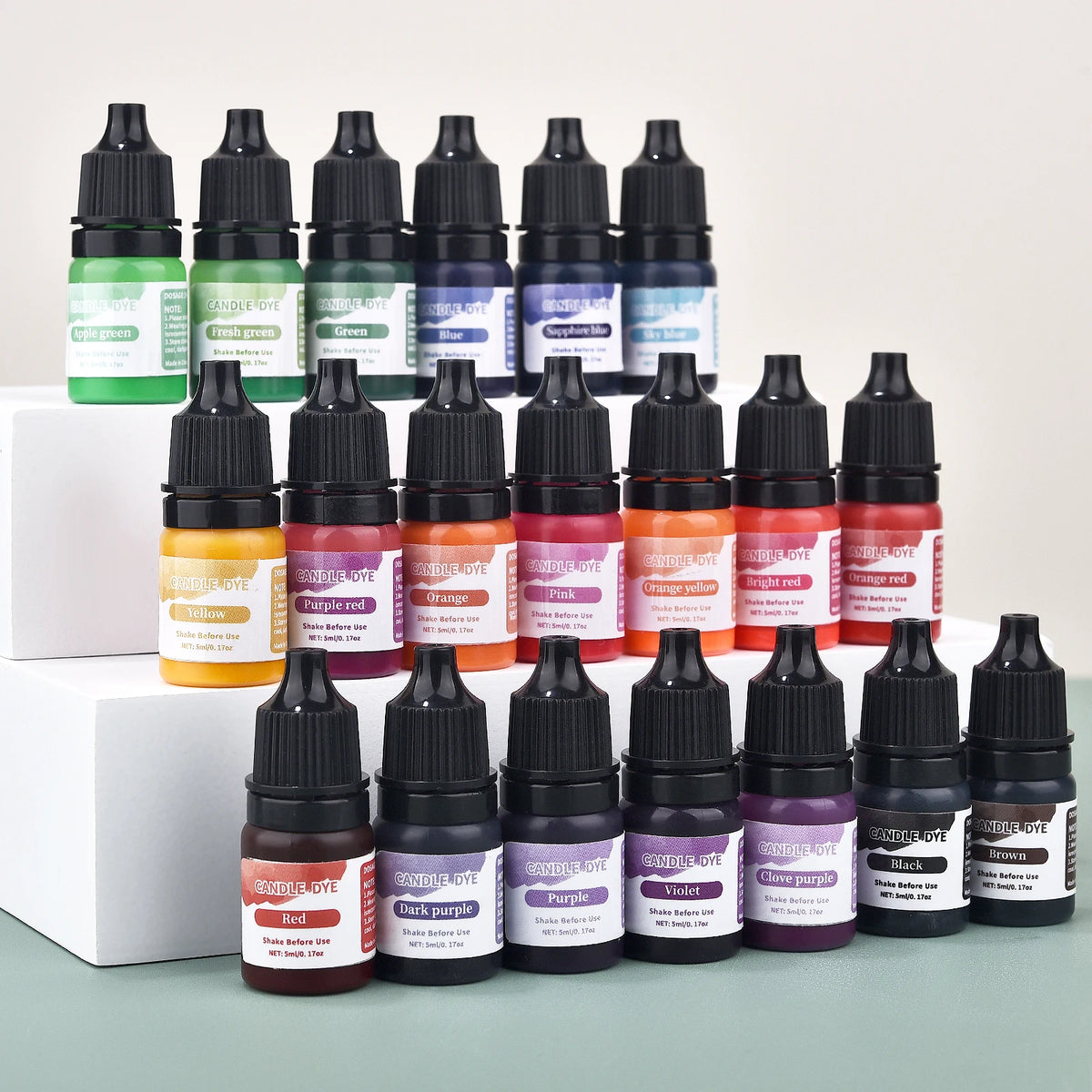 A collection of dark glass dropper bottles filled with various liquid candle and soap colorants in shades of green, yellow, p