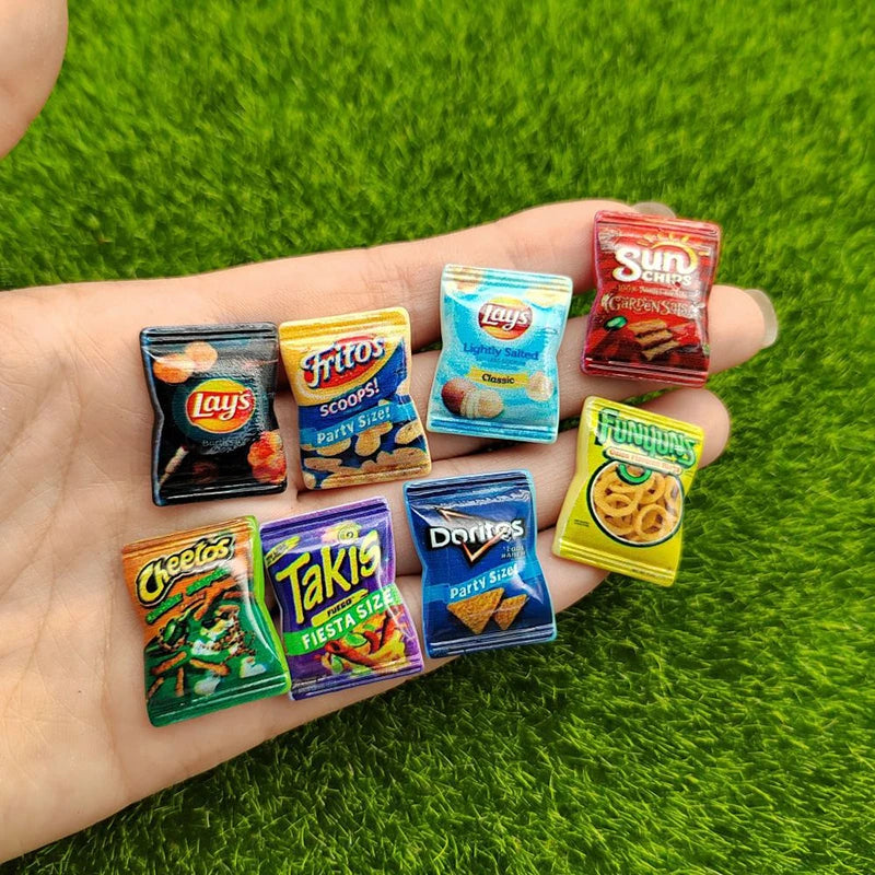 A hand holds a set of ten colorful potato chip snacks including Lay's, Fritos, Doritos, and Sun Chips on a green surface.