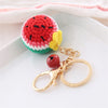 A handmade crochet watermelon fruit pendant keychain with a yellow stem resting on a white plate.
