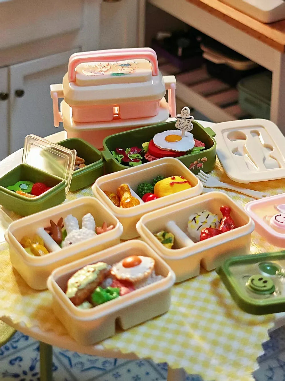 A collection of miniature doll picnic lunch boxes in various pastel colors and shapes arranged on a yellow checkered cloth.