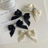 A collection of black and ivory satin ribbon bows adorned with silver rhinestones, displayed next to a perfume bottle.