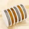 A set of white spools of stainless steel beading wire in various shades of gold and silver.