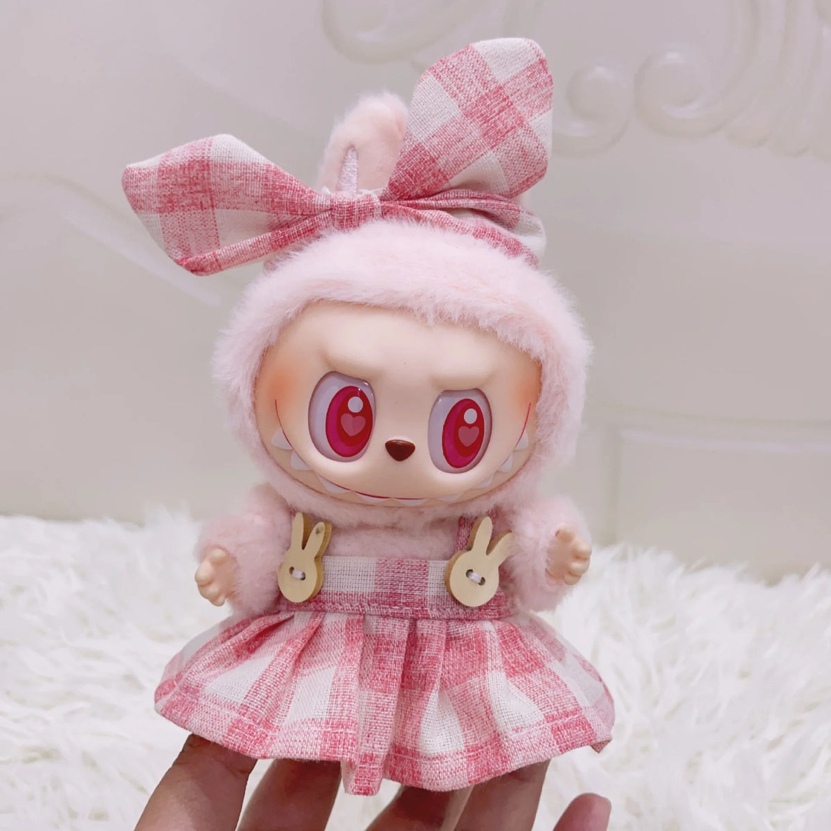 A cute doll wearing a pink and red plaid outfit with a matching bow and fluffy pink hair.