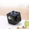A black fidget cube with a rotating joystick and magnetic buttons resting on a white surface.