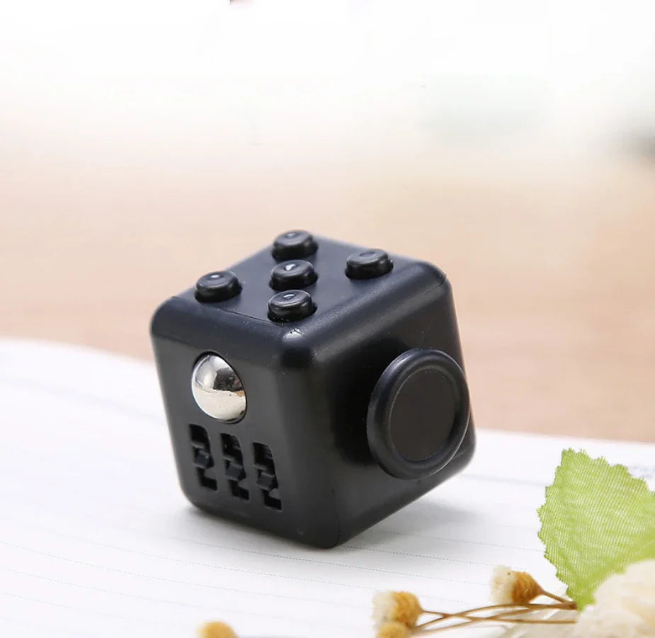 A black fidget cube with a rotating joystick and magnetic buttons resting on a white surface.