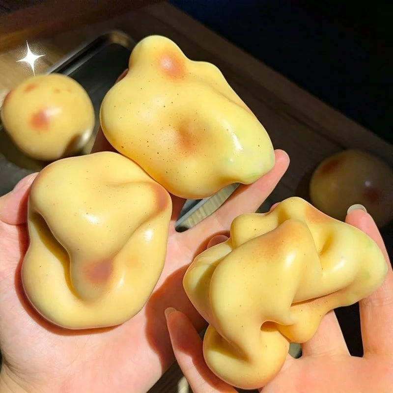 A hand holds a yellow, squishy potato stress ball fidget toy against a dark background.