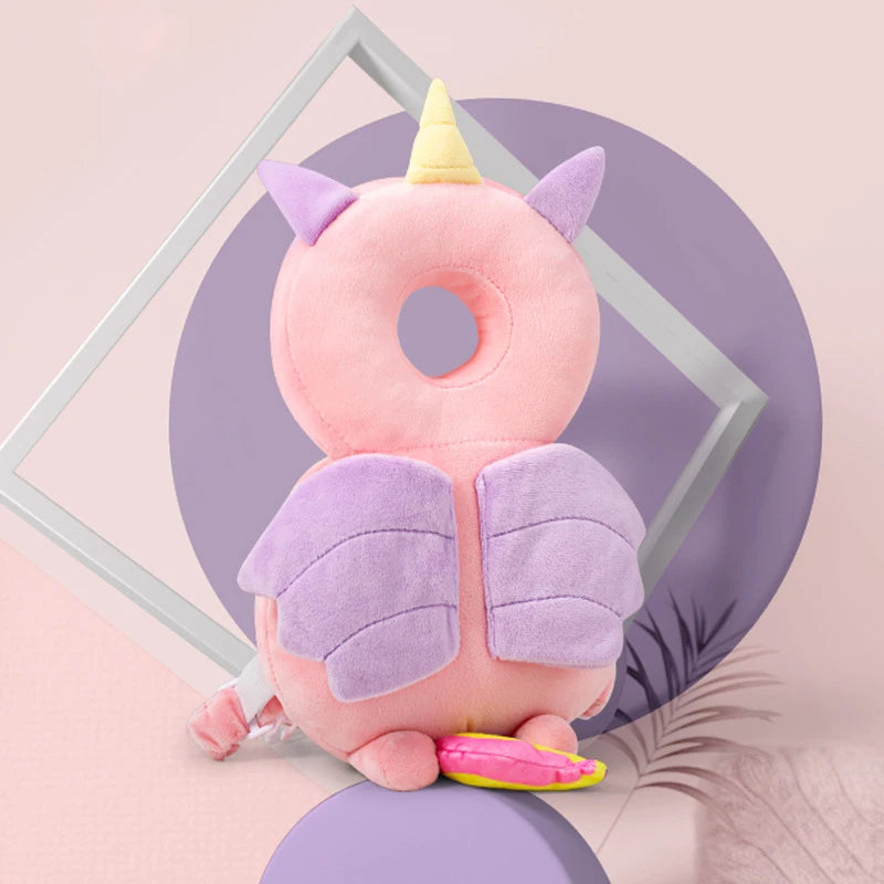 A pink unicorn-themed soft baby head protector pillow with purple wings and a yellow horn.