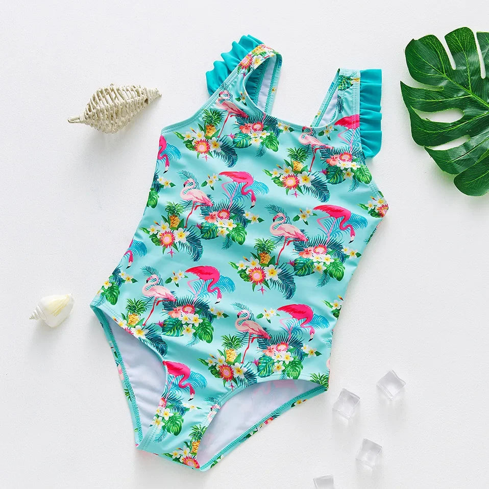 A turquoise kids one-piece swimsuit featuring a vibrant pattern of pink and green tropical flowers and birds.