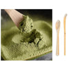 A set of traditional bamboo matcha whisks shown next to a pile of green matcha powder.
