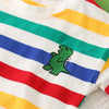 A white t-shirt with horizontal stripes of red, blue, green, and yellow, featuring a small green dinosaur graphic.