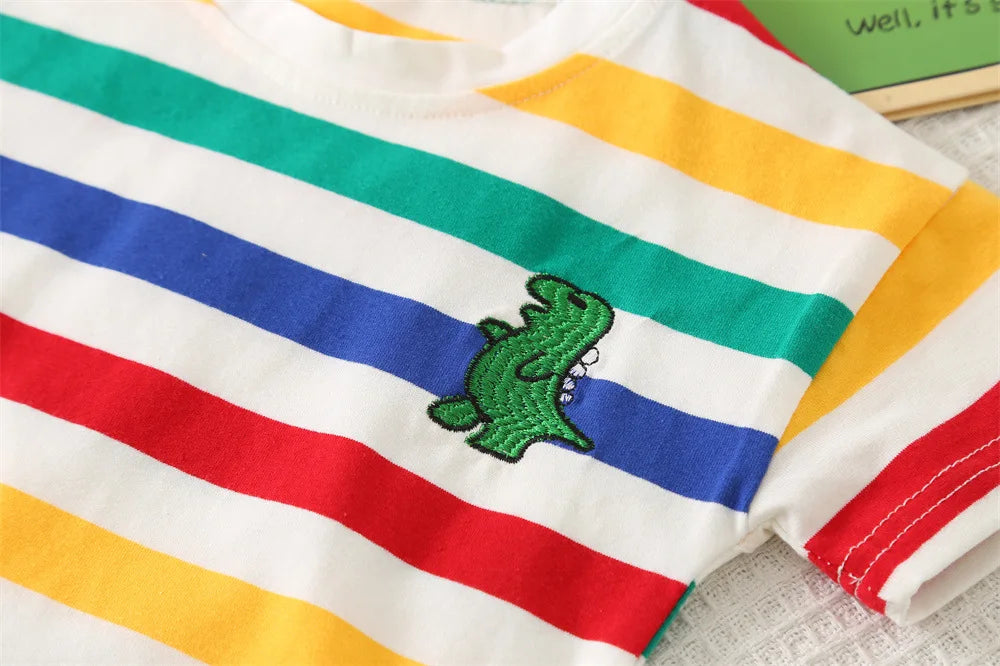 A white t-shirt with horizontal stripes of red, blue, green, and yellow, featuring a small green dinosaur graphic.